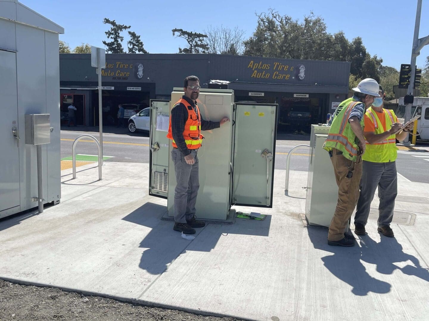 Workers inspecting electrical boxes on sidewalk.