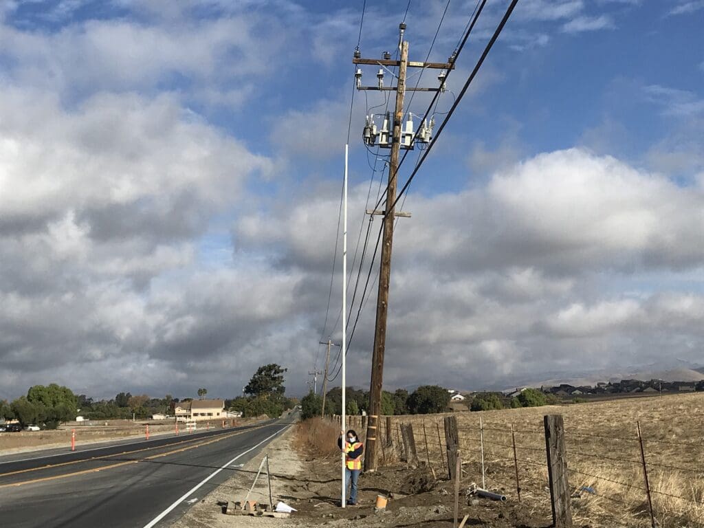 Worker installing pole beside rural road.