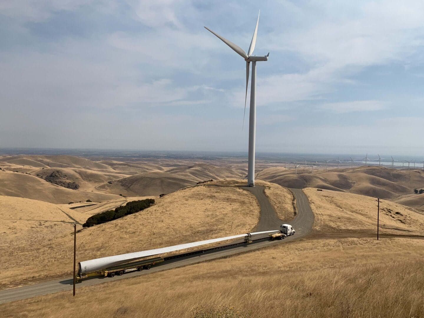 Truck hauling wind turbine blade in landscape.
