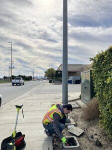Worker checking utility box on sidewalk.